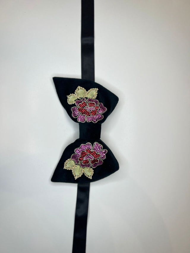 A black bow tie with embroidered floral patterns in pink, red, and gold on a plain white background.