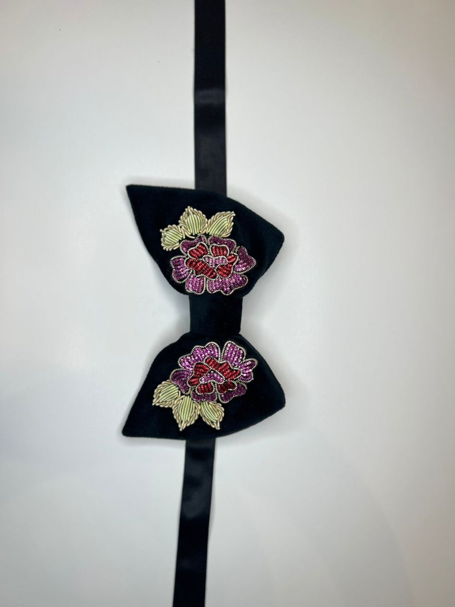 A black bow tie with embroidered floral patterns in pink, red, and gold on a plain white background.