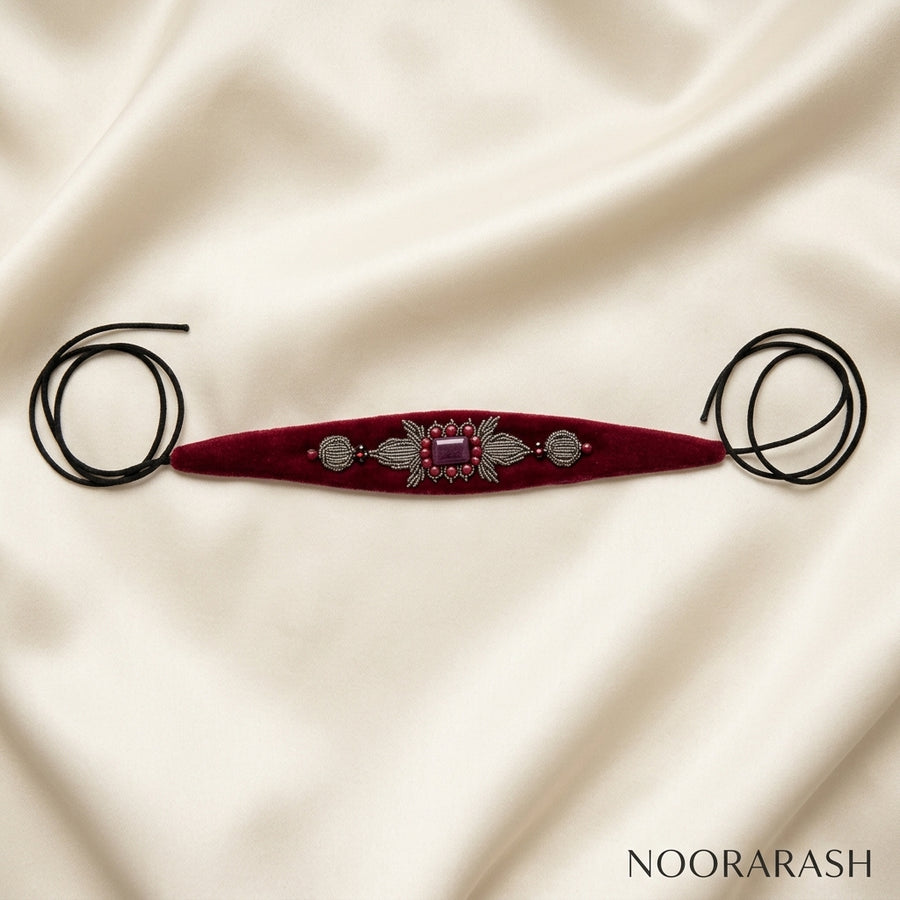 Burgundy velvet Zinat choker necklace with silver and pink crystal embellishments, laid flat with long cord ties on draped cream satin fabric.