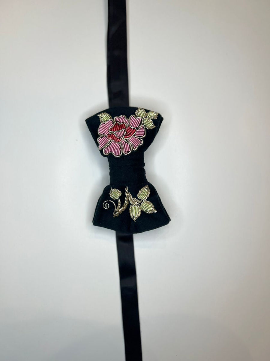 A black bow tie with intricate floral embroidery in pink, red, and gold on the front, hanging against a plain white background.