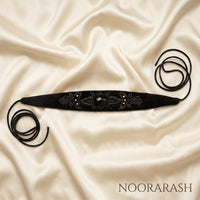Black velvet Zinat choker necklace with black beaded embroidery and a central faceted stone, laid flat with long cord ties on cream satin fabric.