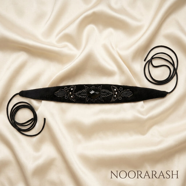 Black velvet Zinat choker necklace with black beaded embroidery and a central faceted stone, laid flat with long cord ties on cream satin fabric.