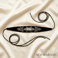 Black velvet Zinat choker necklace with intricate silver floral embroidery and beaded details, laid flat with long ties on draped cream satin fabric.