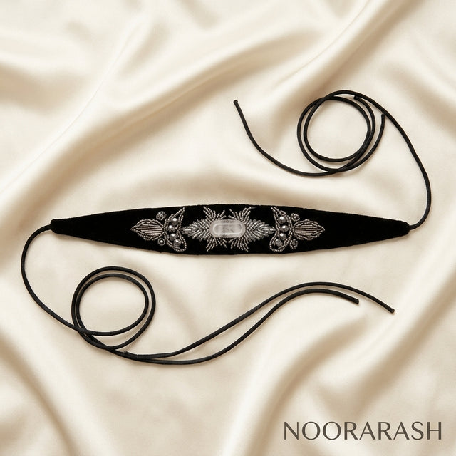 Black velvet Zinat choker necklace with intricate silver floral embroidery and beaded details, laid flat with long ties on draped cream satin fabric.