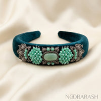 A dark teal velvet cuff bracelet with ornate silver filigree and clusters of mint green beads, displayed on a draped cream satin fabric. The brand name 'NOORARASH' is visible in the bottom right corner.