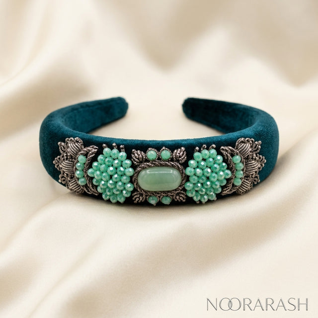 A dark teal velvet cuff bracelet with ornate silver filigree and clusters of mint green beads, displayed on a draped cream satin fabric. The brand name 'NOORARASH' is visible in the bottom right corner.