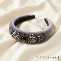 A wide lavender-gray velvet headband decorated with silver bead clusters, floral embroidery, and a central black gemstone, displayed on draped cream satin fabric. The brand name NOORARASH is printed in the bottom right corner.