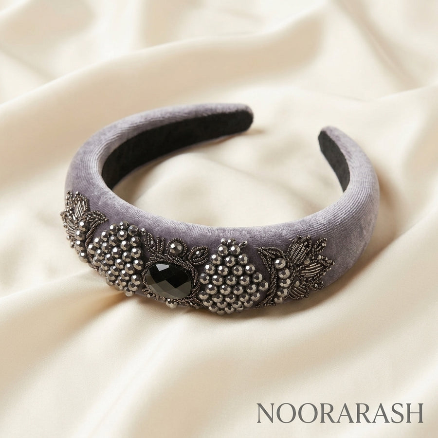 A wide lavender-gray velvet headband decorated with silver bead clusters, floral embroidery, and a central black gemstone, displayed on draped cream satin fabric. The brand name NOORARASH is printed in the bottom right corner.