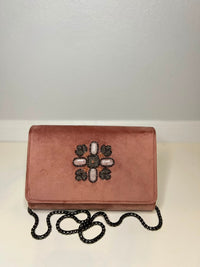 A dusty rose velvet clutch bag with a black beaded chain strap and a decorative floral embellishment on the front, set against a plain light gray background.