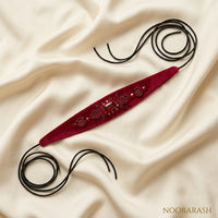 Deep red velvet Zinat choker necklace with intricate beadwork and gold-toned embellishments, laid flat with long cord ties on draped cream satin fabric.